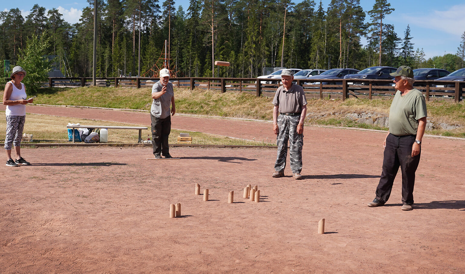 Ikäihmiset heittämässä mölkkyä urheilukentällä.